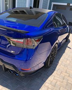 the rear end of a blue car parked in front of a house with two garage doors