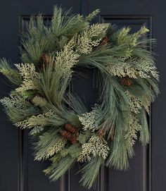 a wreath with pine cones and needles hanging on a black front door, ready for christmas