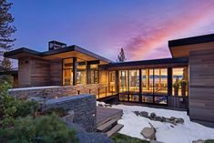 the exterior of a modern home at dusk with snow on the ground and rocks in front