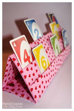 an origami table top with numbers and hearts on pink paper folded to look like a card holder