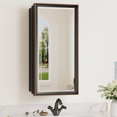 a bathroom sink sitting under a mirror next to a vase with flowers on top of it