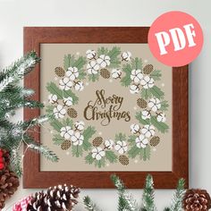 a cross stitch christmas wreath with pine cones and evergreen leaves on the side, surrounded by pine cones