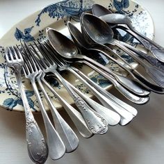 an assortment of spoons and forks on a blue floral plate with white flowers in the background