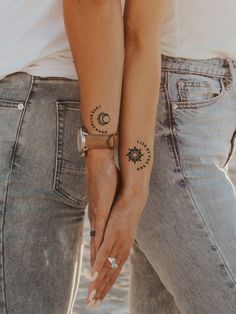 two people holding hands with tattoos on their arms and the other one has a sun and moon tattoo