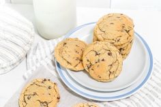 chocolate chip cookies on a white plate next to a glass of milk and a striped towel