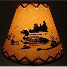 a lamp shade that has a duck in the water on it's side with trees and grass around it