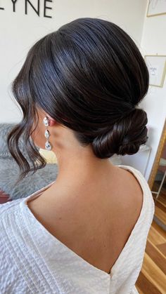 a woman with black hair wearing earrings and a white top is looking at the wall