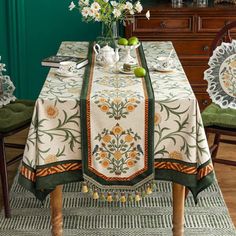 a dining room table covered with a white and green tablecloth next to two chairs