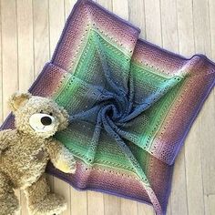 a brown teddy bear sitting on top of a purple and green crocheted blanket