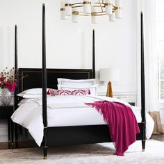 a bedroom with four post bed, white walls and pink throw blanket on the floor