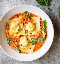 a white plate topped with ravioli and spinach covered in sauce on top of a table