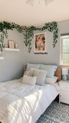 a white bed sitting under a window next to a plant covered wall in a bedroom