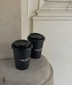 two black coffee cups sitting on top of a cement pillar next to a white door