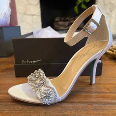 a pair of white high heeled shoes sitting on top of a wooden table next to a box