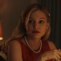 a woman in a red dress is smiling and looking at the camera with pearls on her necklace