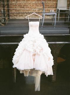 a wedding dress hanging on a rack in front of a brick wall with chairs around it