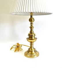 a gold lamp with a white shade on it and a cord attached to the base