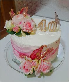 a white cake with pink flowers and gold numbers on top is sitting on a glass plate