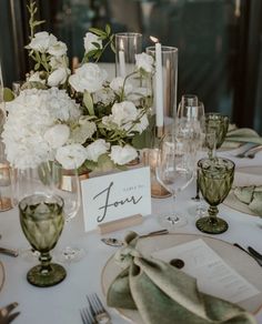 the table is set with white flowers and place cards for guests to sit down at