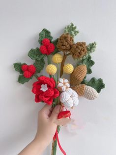 a hand holding a bunch of crocheted flowers on top of a white wall