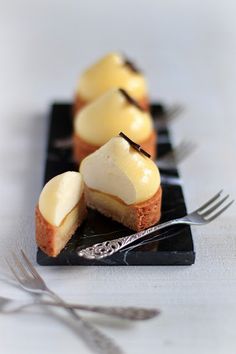 three small desserts are sitting on a black plate with silverware next to them