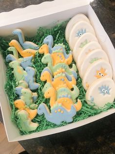 decorated cookies in a box with green grass and blue dinosaurs on them for a baby's first birthday