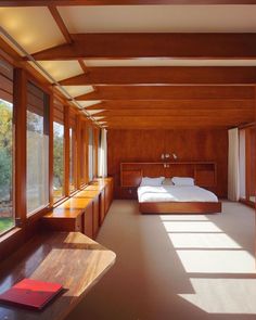 a bed sitting in a bedroom next to windows and a wooden table with a book on it