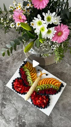 a vase filled with flowers and fruit on top of a marble table next to a cutting board