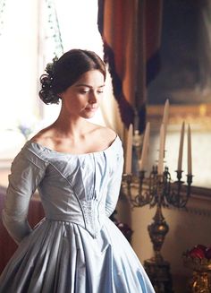 a woman in a blue dress standing next to a window