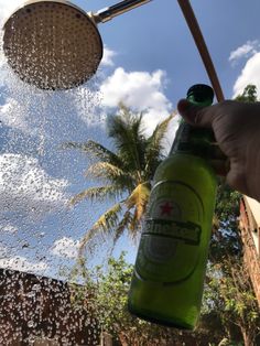 a person is holding a green bottle in front of a shower head and palm trees