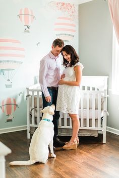 a man and woman standing next to a white dog in a room with hot air balloons on the wall