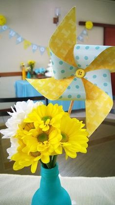 a blue vase filled with yellow flowers and a pinwheel on top of a table