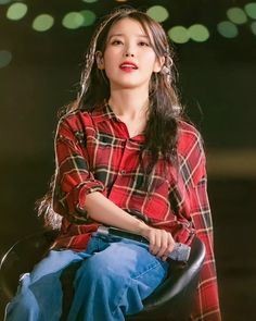 a woman sitting on top of a chair wearing a red plaid shirt and blue jeans