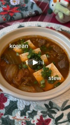 a bowl of soup with tofu and green onions in it on a floral table cloth