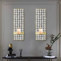 two wall sconces with candles on them in front of a table and vase