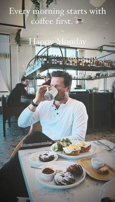 a man drinking coffee while sitting at a table with food and drinks in front of him