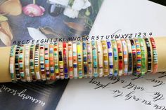 a stack of colorful bracelets sitting on top of an open book next to flowers