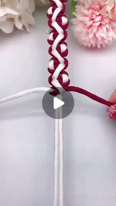 someone is making a braided bracelet with red and white beads on the end, next to pink flowers