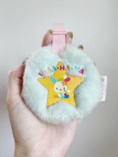 a hand holding a small stuffed animal with a star on it's back and name tag