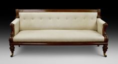 a white couch with wooden frame and buttons on the armrests, sitting in front of a black background