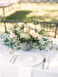 a table with white flowers and greenery on it is set for an outdoor dinner