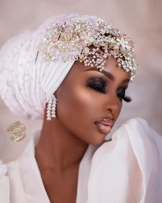 a woman wearing a white turban with pearls on her head and black eyeliners