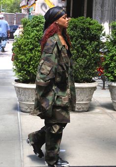 a woman with red hair is walking down the street wearing camouflage clothing and black sneakers