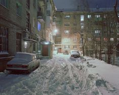 a snowy street with cars parked on the side and buildings in the background at night