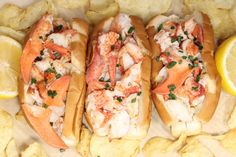 two lobster sandwiches with potato chips and lemon wedges