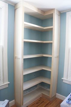 an empty room with blue walls and white trim on the shelves, along with wood flooring