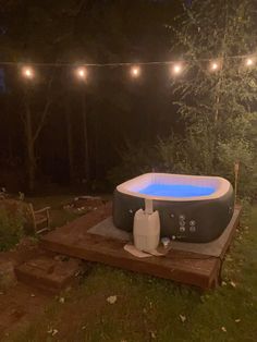 an inflatable hot tub is lit up at night with string lights above it