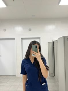 a woman in scrubs is taking a selfie with her cell phone while standing in the bathroom