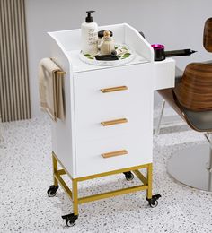 a white cabinet with gold handles on wheels and a wooden chair in the corner behind it