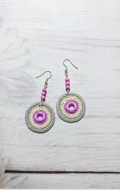 two circular crocheted earrings with pink and yellow beads on them, sitting on a white wooden surface